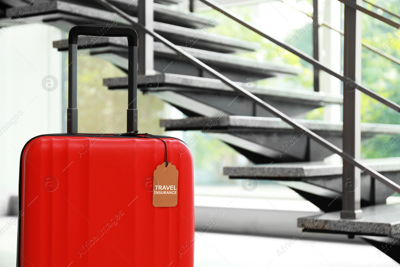 Photo of Red suitcase with TRAVEL INSURANCE label at stairs indoors, space for text