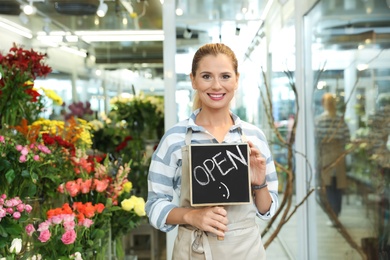 Photo of Female florist holding sign "OPEN" in flower shop