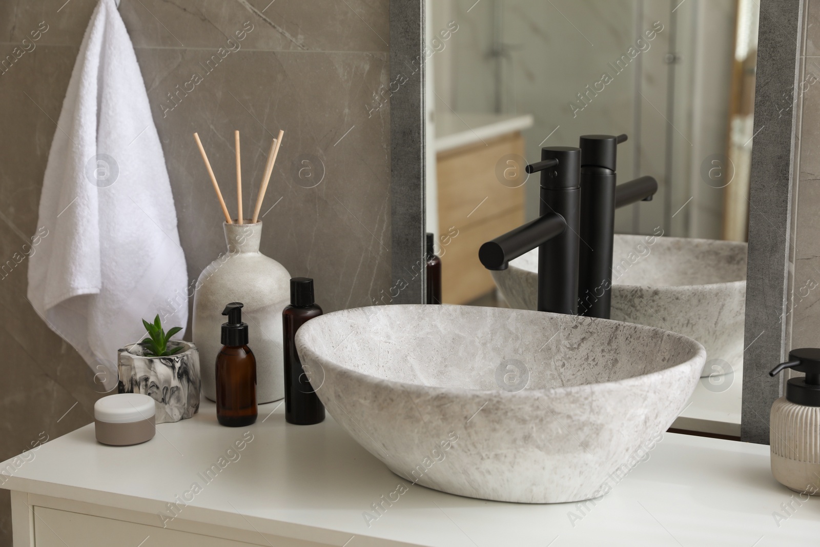 Photo of Stone vessel sink with faucet and toiletries on white countertop in bathroom