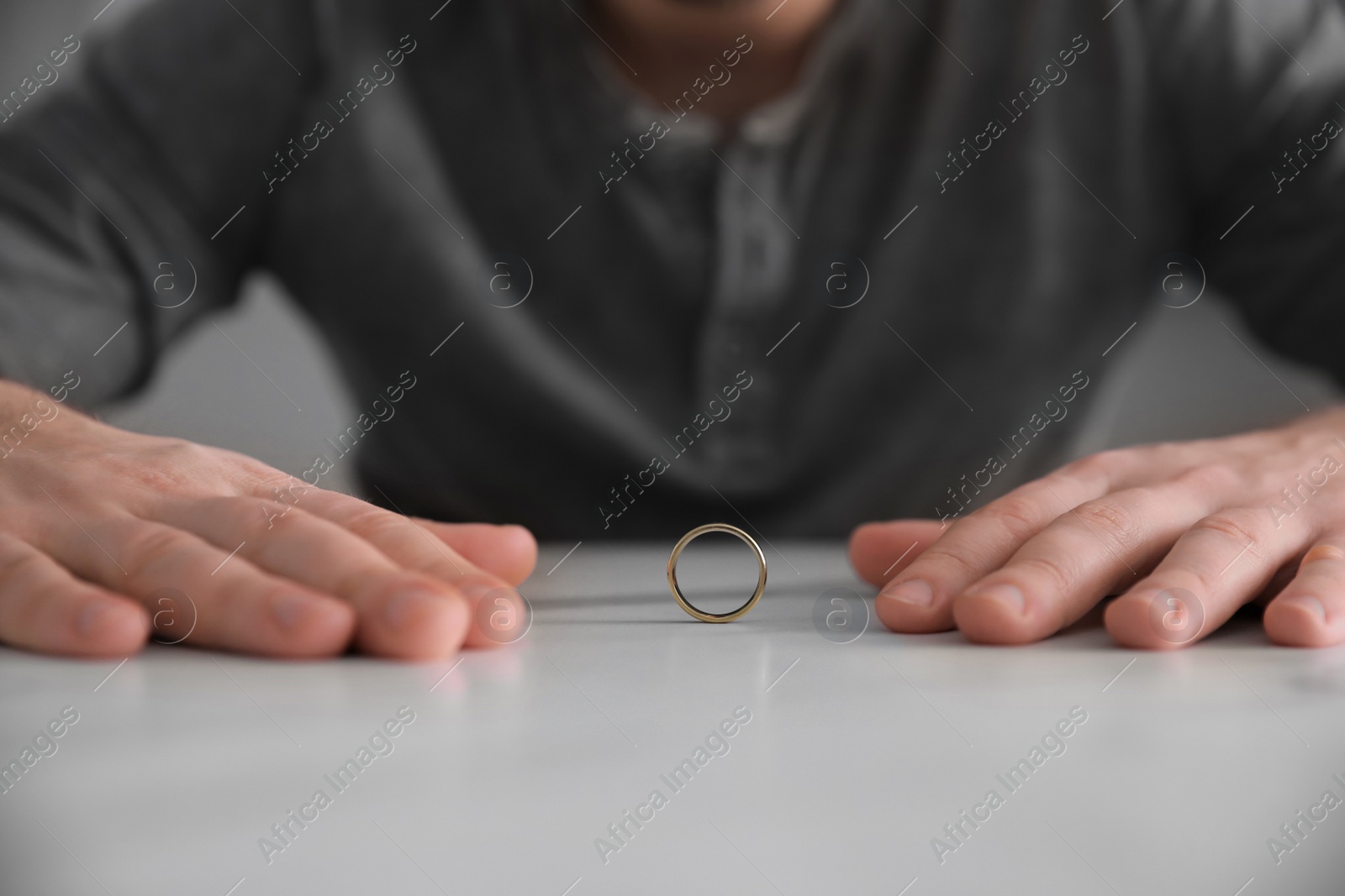 Photo of Man with wedding ring at white table, closeup. Divorce concept