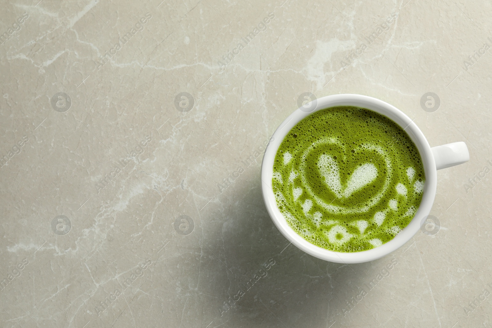 Photo of Delicious matcha latte in cup on marble table, top view. Space for text