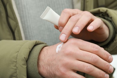 Man applying cream from tube onto hand, closeup. Winter care