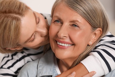 Daughter kissing her mature mother on cheek indoors