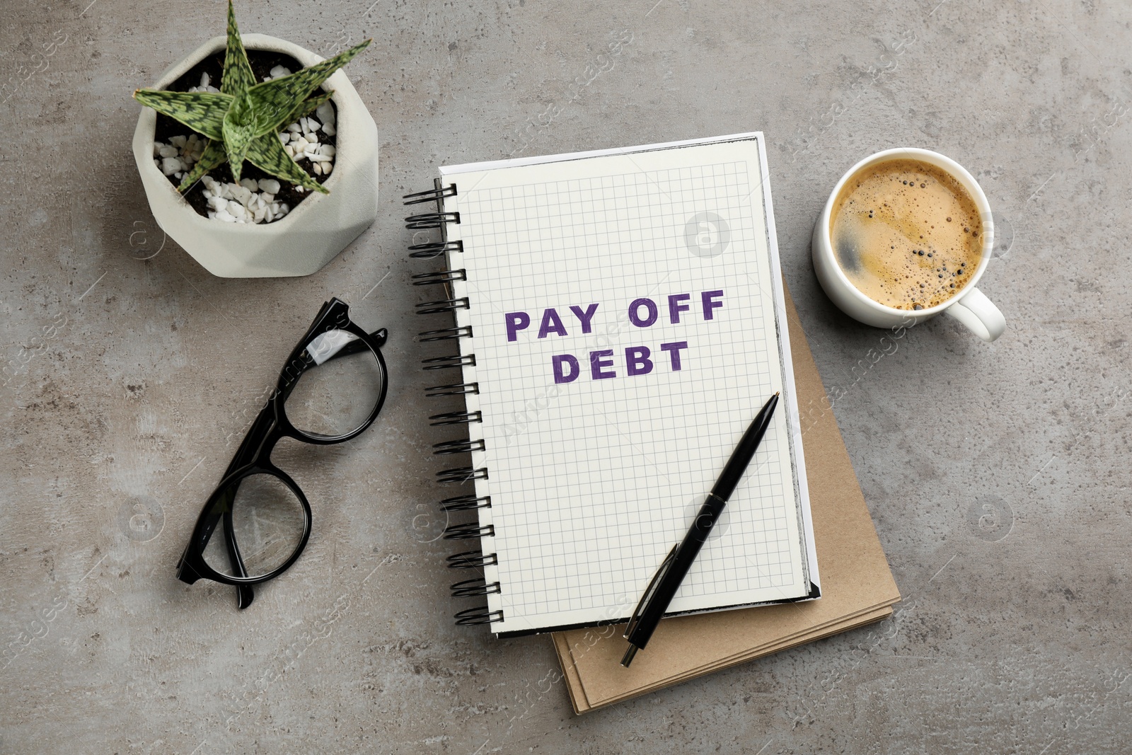 Image of Notebook with phrase Pay Off Debt, cup of aromatic coffee and plant on grey table, flat lay