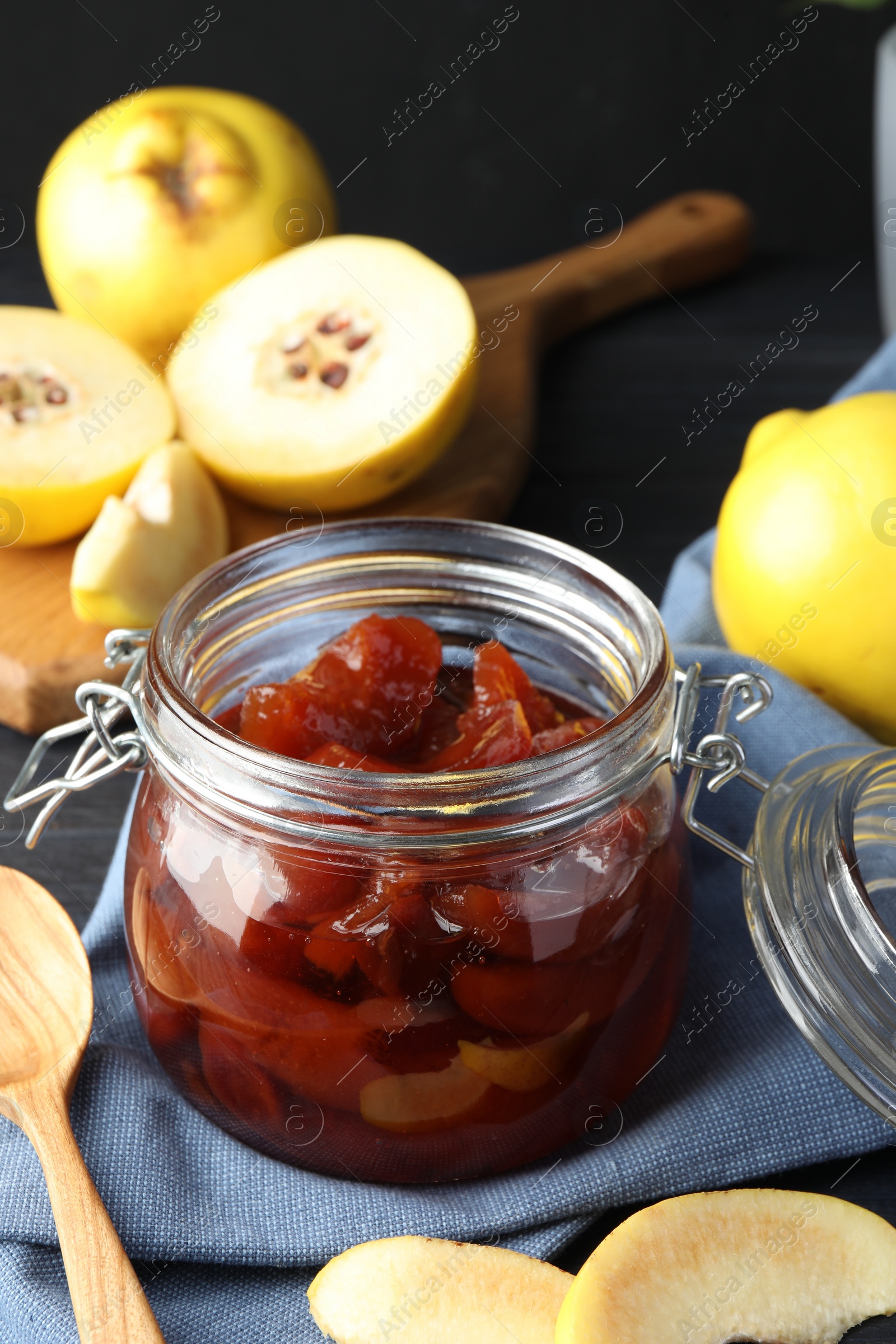 Photo of Quince jam in glass jar, spoon and fresh raw fruits on grey table, closeup