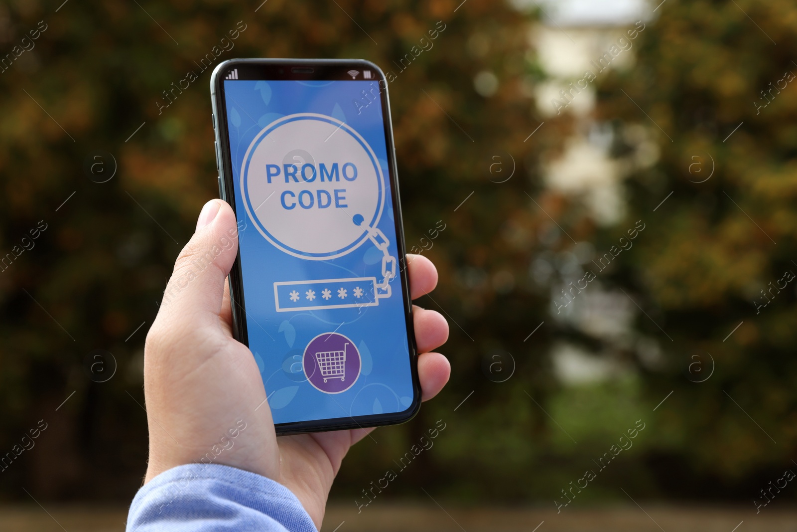 Photo of Man holding smartphone with promo code near trees outdoors, closeup. Space for text