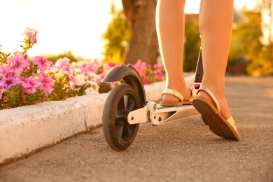 Woman riding electric kick scooter outdoors on sunny day, closeup