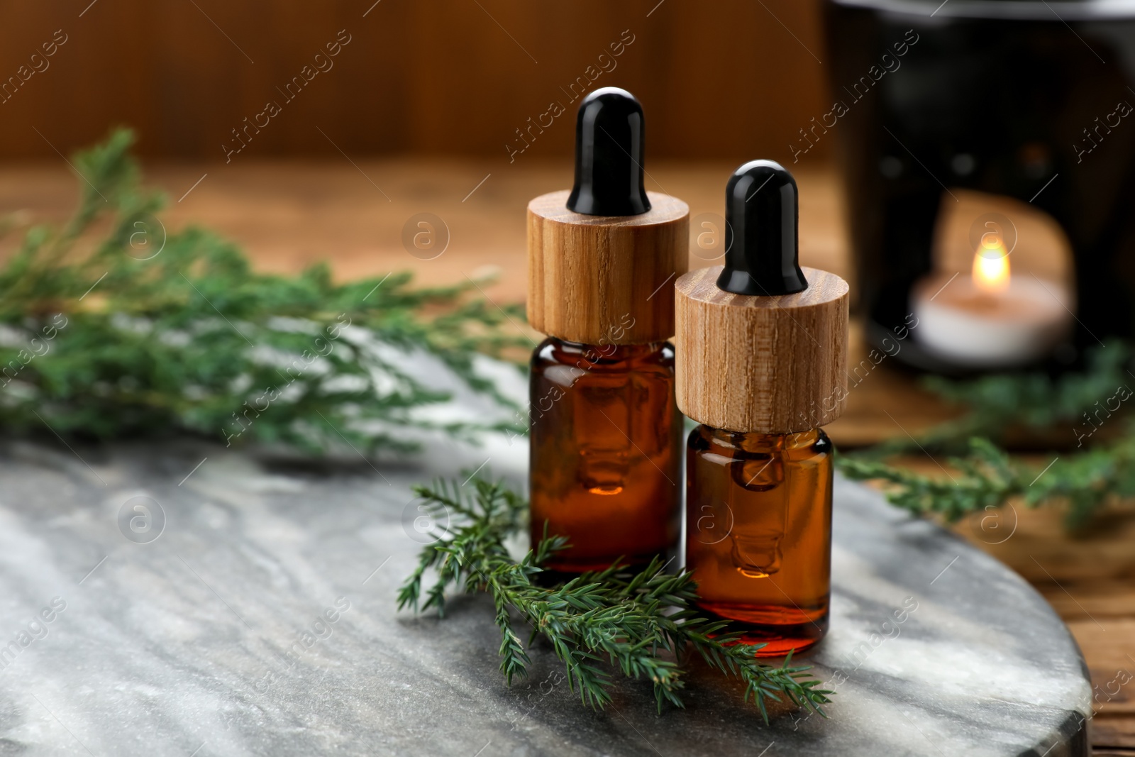 Photo of Bottles of juniper essential oil and twigs on wooden table, closeup