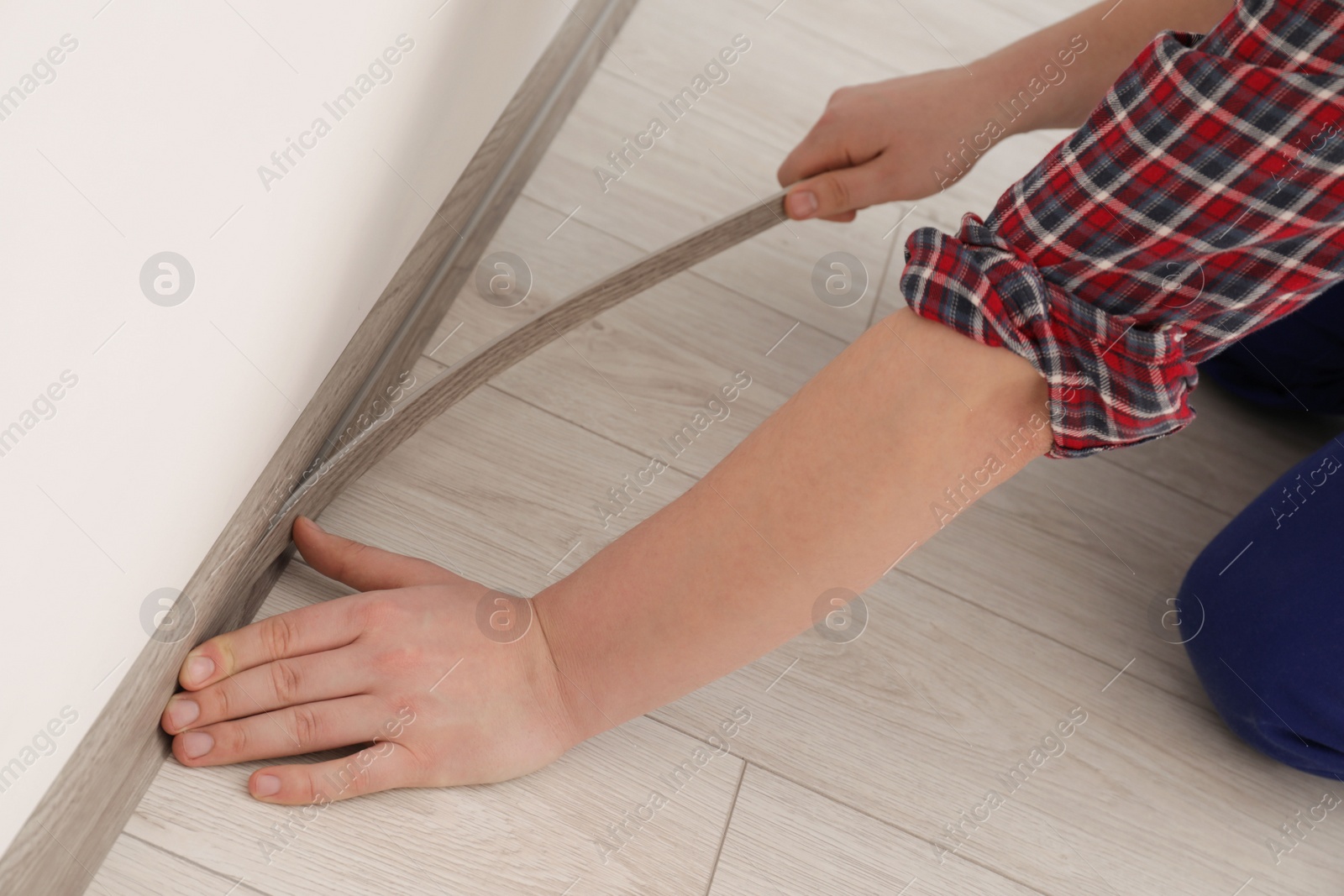 Photo of Man installing plinth on laminated floor in room, closeup