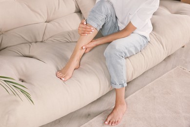 Photo of Woman rubbing sore leg on sofa, closeup