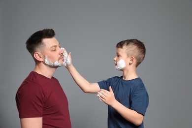 Photo of Son applying shaving foam on dad's face, grey background