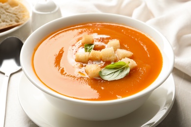 Photo of Bowl of sweet potato soup with croutons and basil served on table, closeup