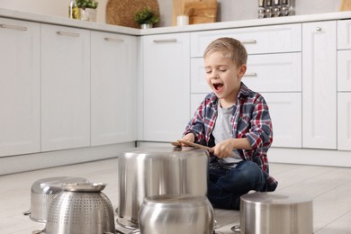 Photo of Little boy pretending to play drums on pots in kitchen