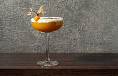 Refreshing cocktail decorated with physalis fruit on wooden table near grey wall. Space for text