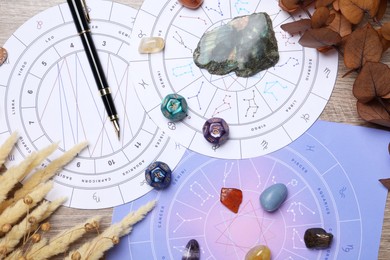 Photo of Zodiac wheels, natal chart, astrology dices, fountain pen and gemstones on wooden table, flat lay