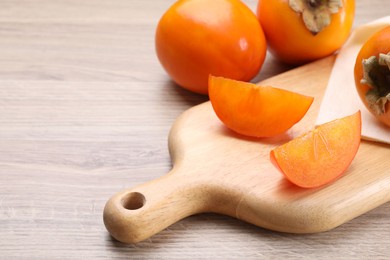 Photo of Delicious ripe persimmons on light wooden table, closeup. Space for text