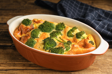 Photo of Tasty broccoli casserole in baking dish on wooden table