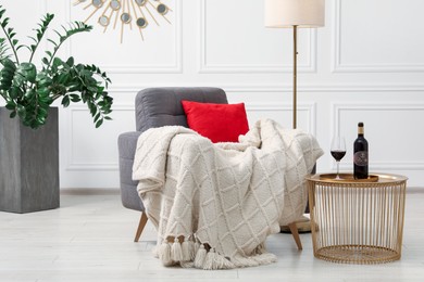 Photo of Stylish living room interior with comfortable armchair, blanket, side table and houseplant