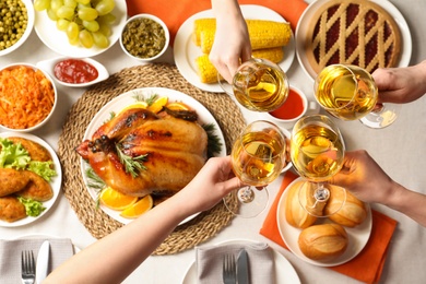 People holding glasses of wine over table with festive dinner and roasted turkey, top view