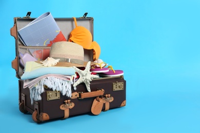 Packed vintage suitcase with different beach objects on light blue background, space for text. Summer vacation
