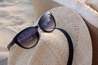 Photo of Hat and bag with beautiful sunglasses on sandy beach, closeup