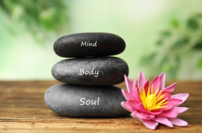 Photo of Stones with words Mind, Body, Soul and lotus flower on wooden table. Zen lifestyle