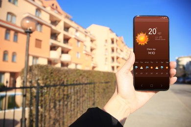 Man using weather forecast app on smartphone outdoors on sunny day, closeup. Data, sun and other illustrations on screen