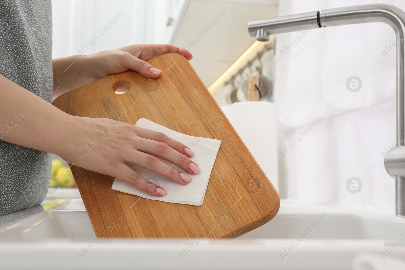 Photo of Woman wiping wooden cutting board with paper napkin at sink in kitchen, closeup