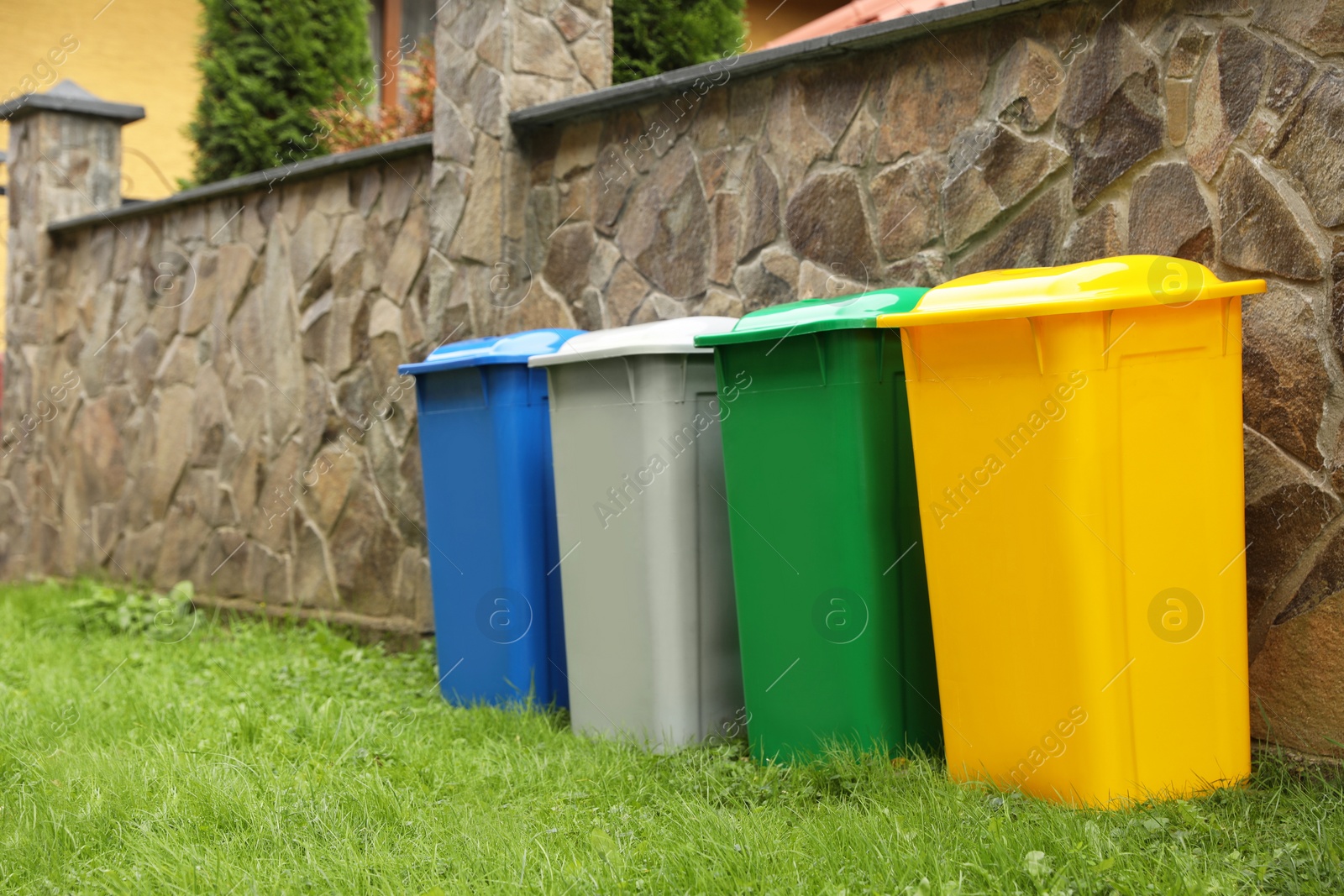 Photo of Many colorful recycling bins near stone fence outdoors