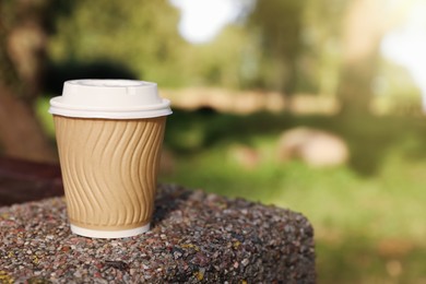 Photo of Paper cup on parapet in park, space for text. Coffee to go