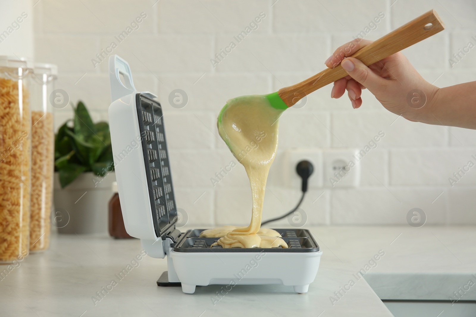 Photo of Woman pouring dough onto Belgian waffle maker in kitchen, closeup