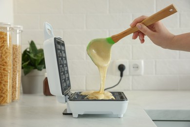 Woman pouring dough onto Belgian waffle maker in kitchen, closeup