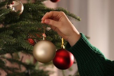 Photo of Woman decorating Christmas tree with beautiful golden bauble, closeup