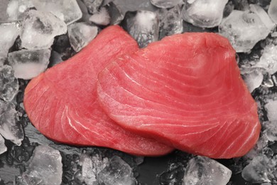 Photo of Raw tuna fillets and ice cubes on dark table, top view