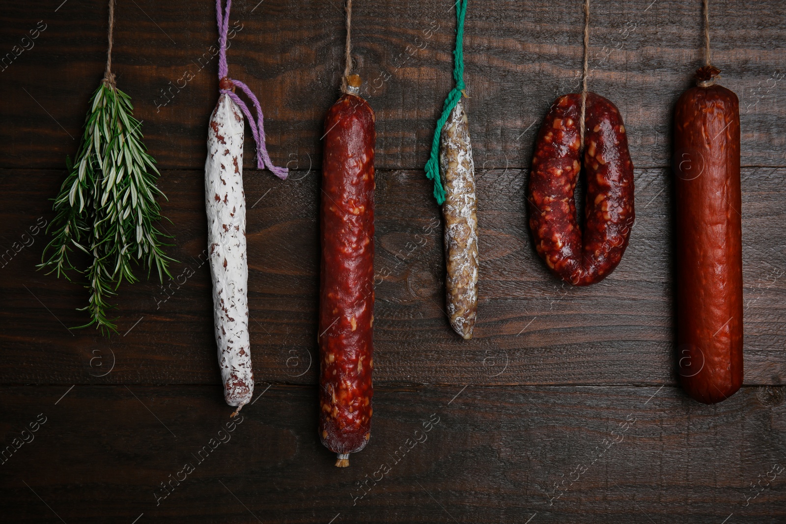 Photo of Different delicious sausages and bunch on rosemary hanging near wooden wall