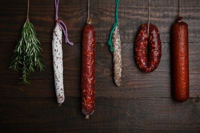 Photo of Different delicious sausages and bunch on rosemary hanging near wooden wall
