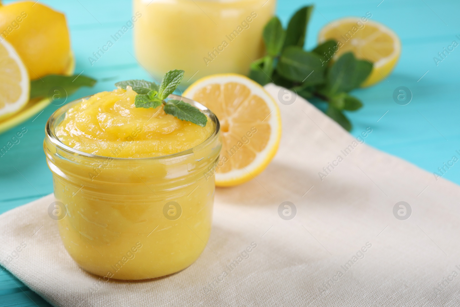 Photo of Delicious lemon curd in glass jar, fresh citrus fruits and mint on light blue table, space for text