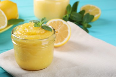 Delicious lemon curd in glass jar, fresh citrus fruits and mint on light blue table, space for text