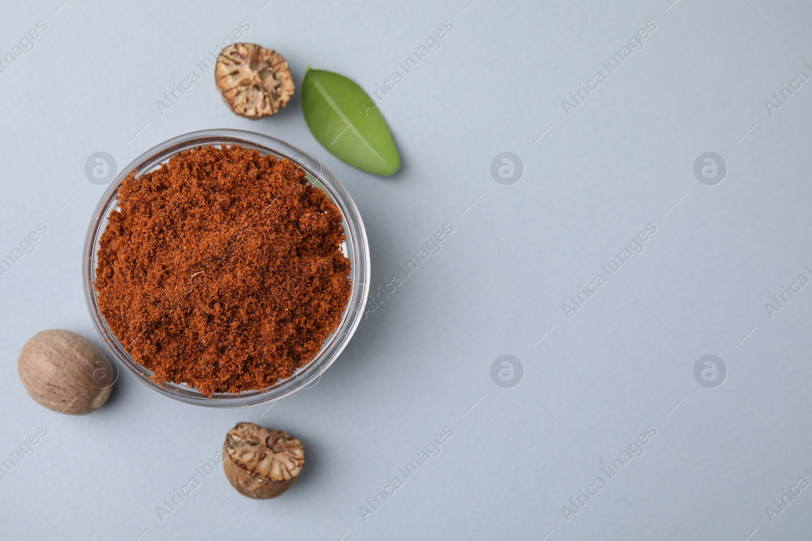 Photo of Nutmeg powder in bowl, seeds and green leaf on white background, flat lay. Space for text