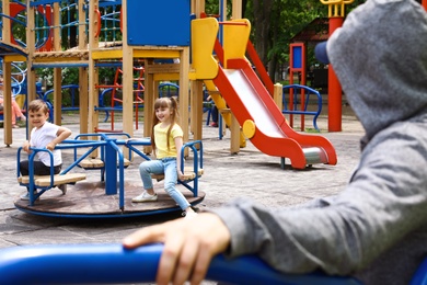 Photo of Suspicious adult man spying on kids at playground, space for text. Child in danger