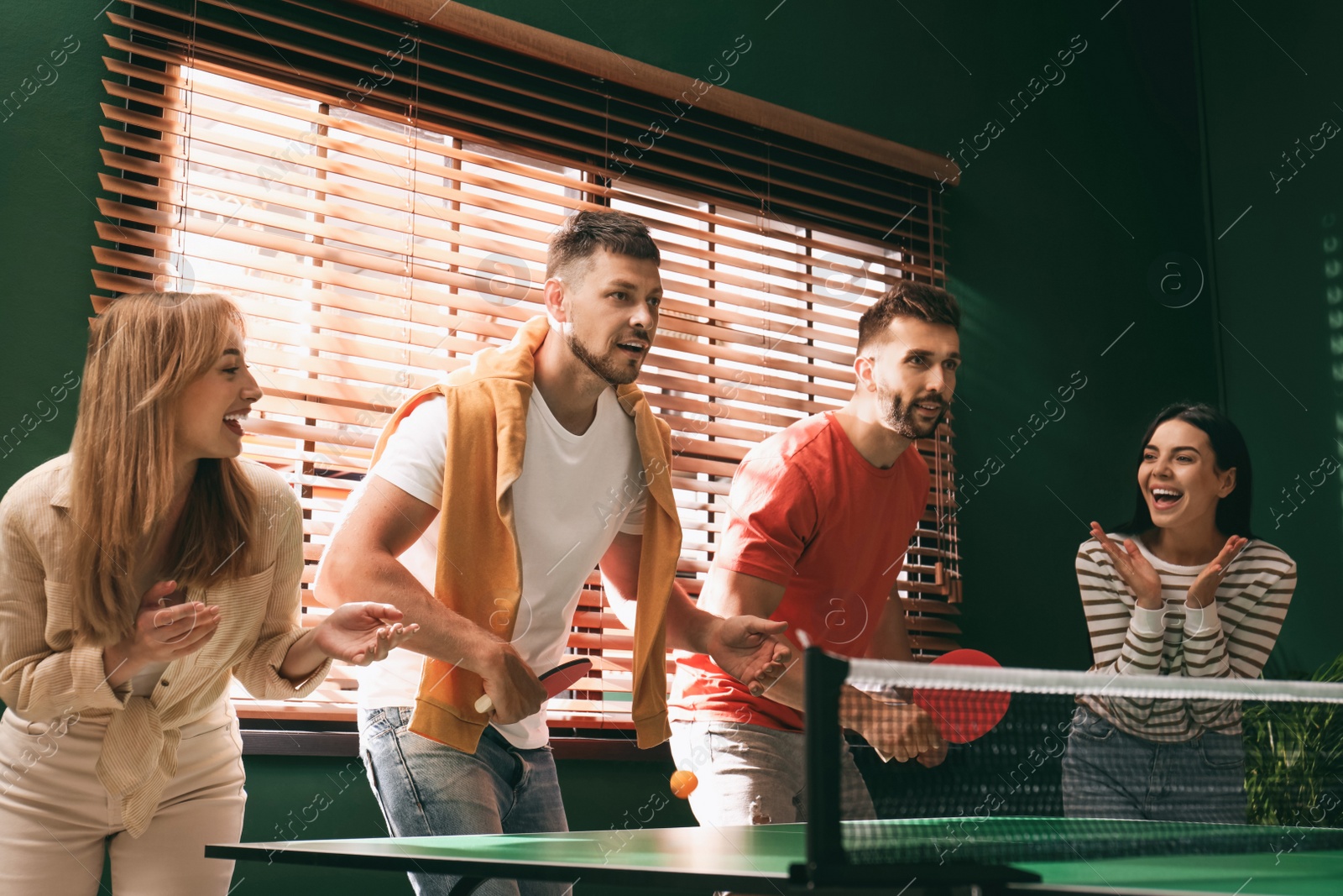 Photo of Happy friends playing ping pong together indoors