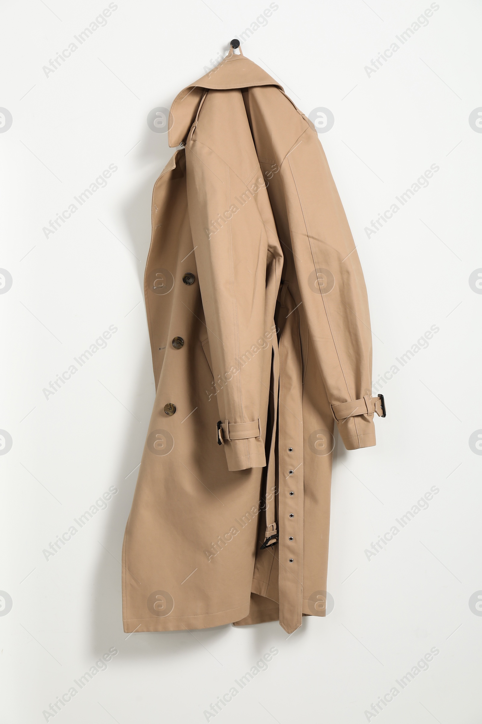 Photo of Beige trench coat hanging on hook rack on white wall