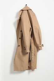 Beige trench coat hanging on hook rack on white wall