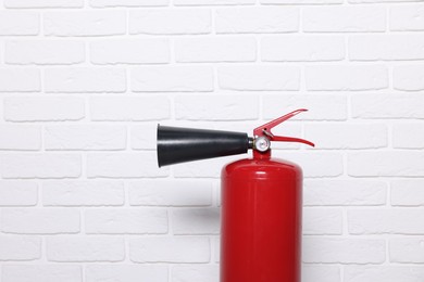 Photo of Red fire extinguisher near white brick wall, space for text
