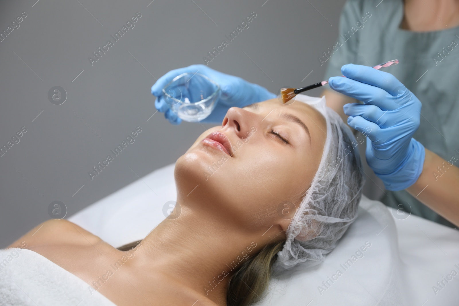 Photo of Cosmetologist applying chemical peel product on client's face in salon