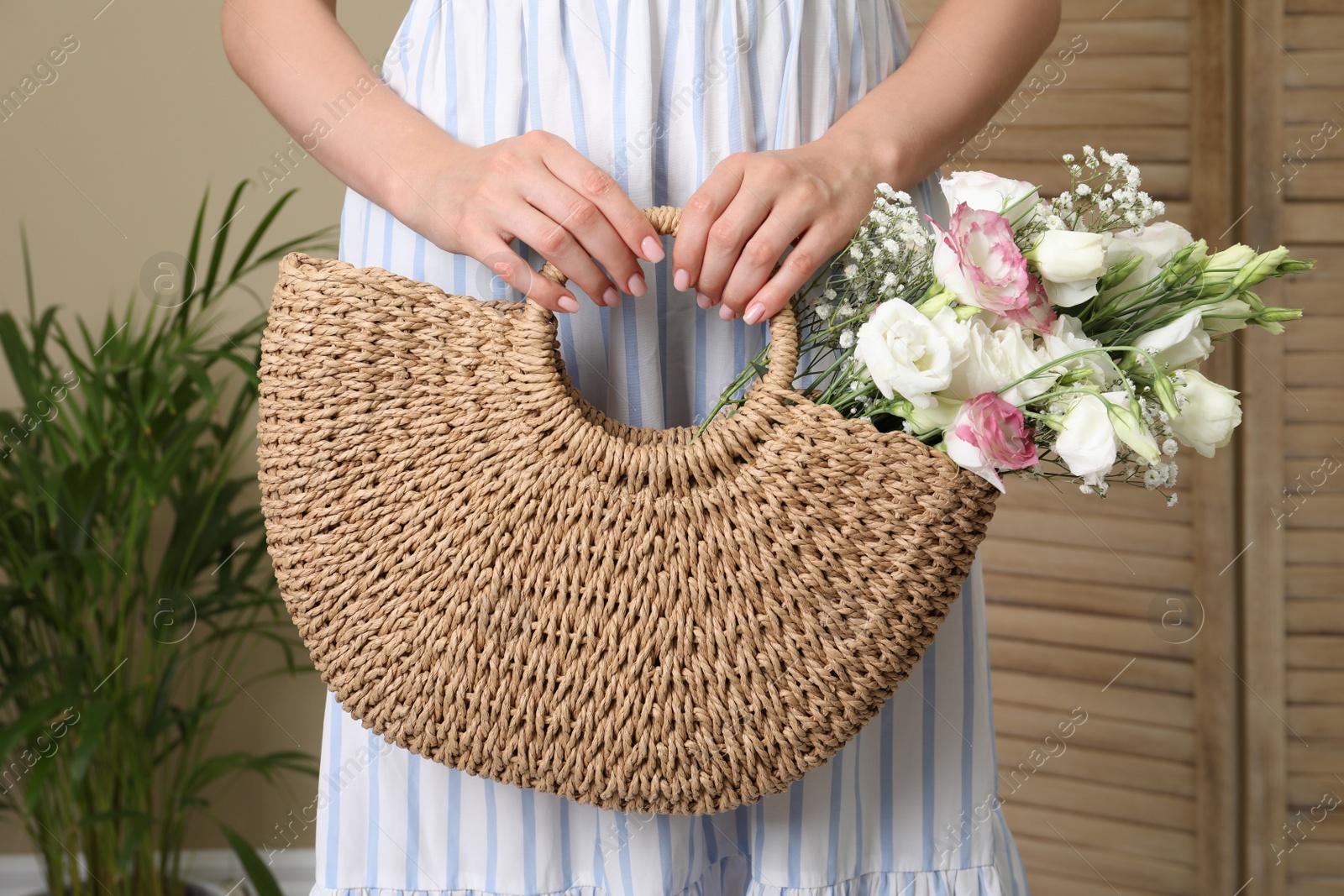 Photo of Woman holding beach bag with beautiful bouquet indoors, closeup