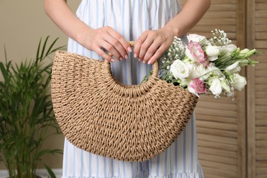 Woman holding beach bag with beautiful bouquet indoors, closeup