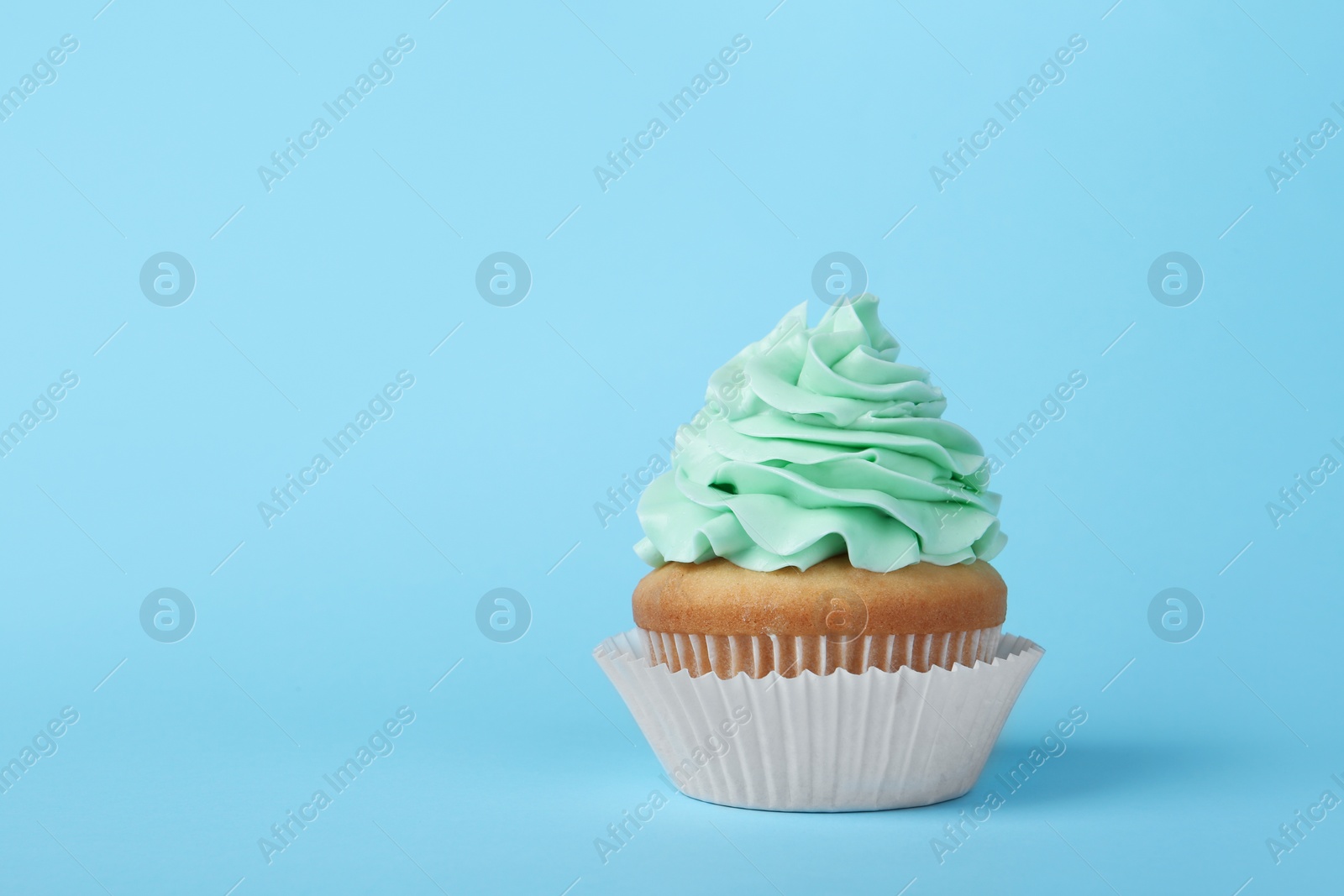 Photo of Tasty cupcake with cream on light blue background, space for text