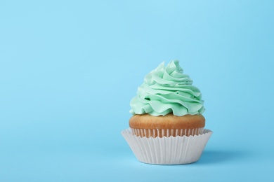 Photo of Tasty cupcake with cream on light blue background, space for text