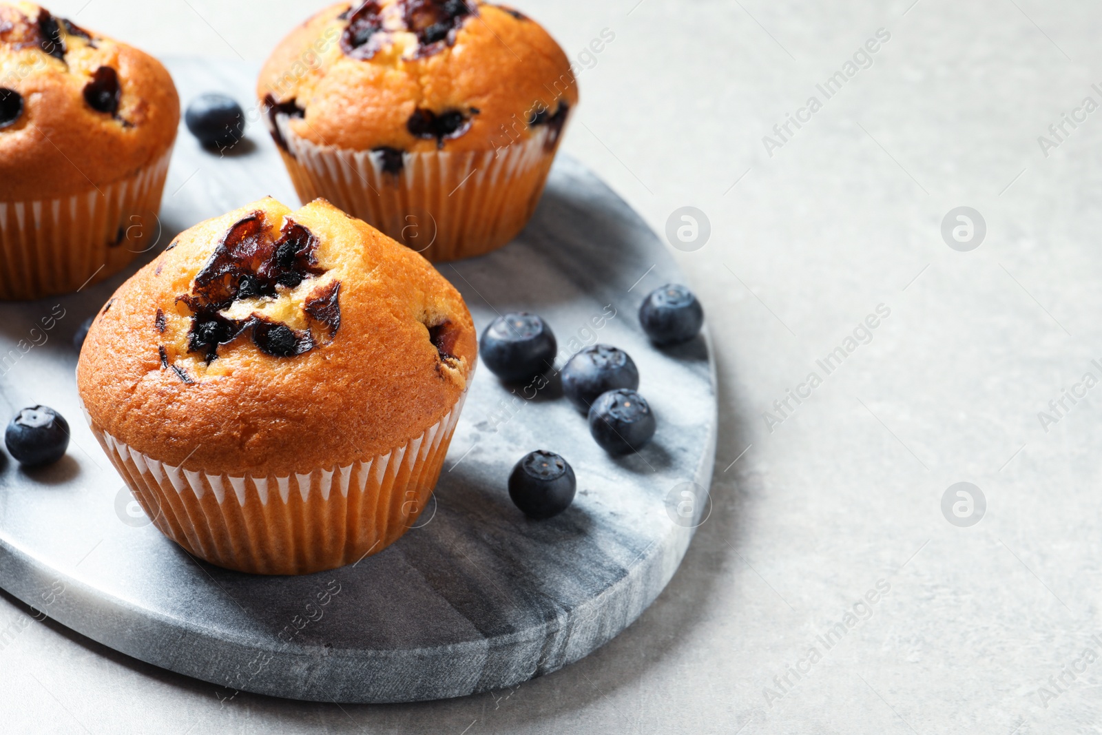 Photo of Stone board with blueberry muffins on light table, closeup view. Space for text